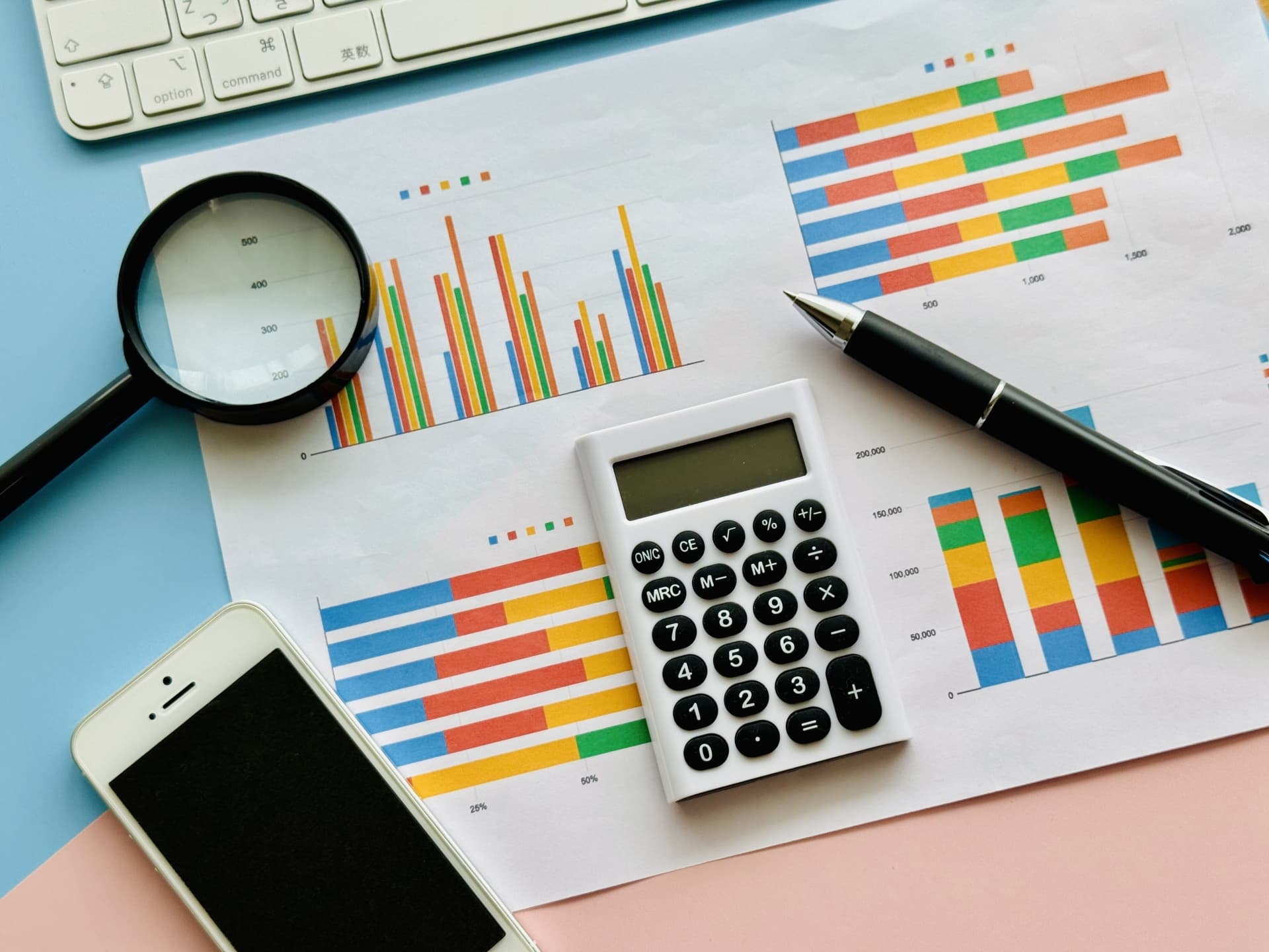 カラフルなグラフと電卓、ボールペン、虫眼鏡